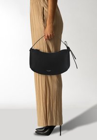 Bolso clutch de cuero negro con forma curva, cierre de cremallera y asa delgada. Presenta un logo sutil en el frente y una superficie texturizada.