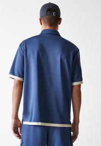 Navy blue short-sleeve polo shirt with a smooth texture, cream-colored accents at the sleeves and hem, and a relaxed fit design.