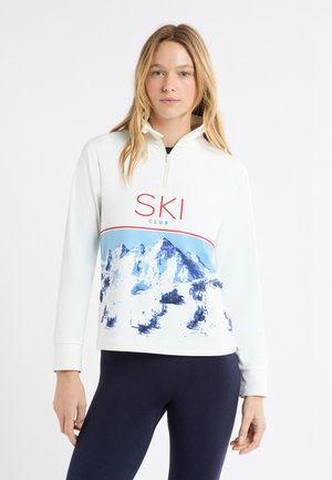 Witte trui met een kwartritssluiting, met een blauw bergmotief en "SKI CLUB" in het rood. Zachte stof met lange mouwen.