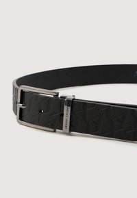 Čierny kožený opasok s embosovaným geometrickým vzorom, striebornou obdĺžnikovou sponou a zapínaním s gravírovaným nápisom "Armani Exchange."