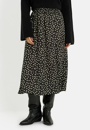 Falda midi negra con lunares blancos, combinada con botas de cuero negras hasta la rodilla y una blusa negra de manga larga con mangas acampanadas.