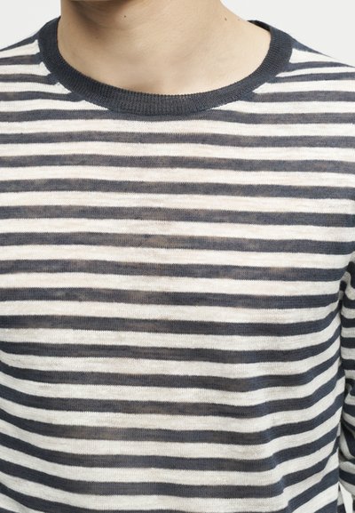 Κοντινό πλάνο από ένα άτομο που φοράει μια μακρυμάνικη μπλούζα με μαύρες και άσπρες οριζόντιες ρίγες και μαύρο ribbed στρογγυλό λαιμό.