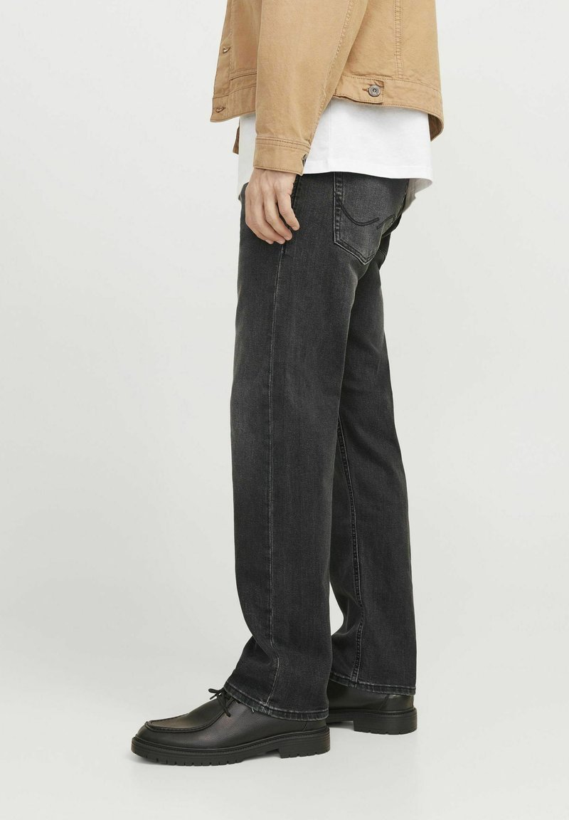 Schwarze Denim-Jeans im geraden Schnitt mit fünf Taschen und minimaler Naht. Kombiniert mit schwarzen Schuhen und einer leichten Jacke.