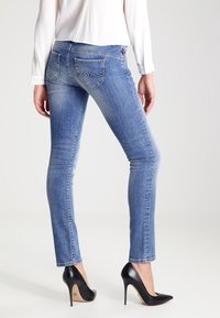 Chude dżinsy w jasnoniebieskim odcieniu z gładką teksturą i ozdobnym przeszyciem tylnych kieszeni. W połączeniu z czarnymi szpilkami.