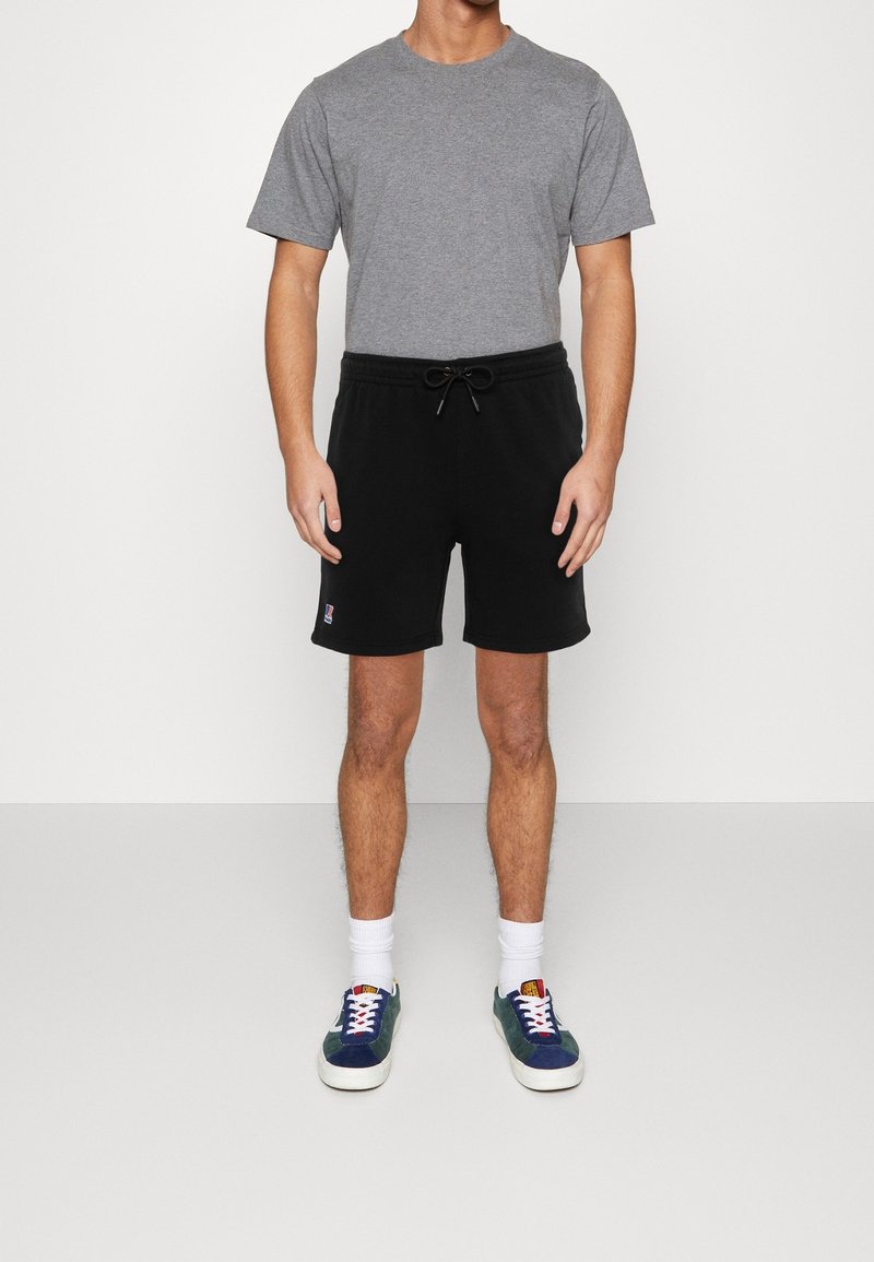 T-shirt gris en coton à manches courtes, associé à un short noir avec cordon de serrage. Chaussures : baskets bleues et vertes avec semelles blanches.