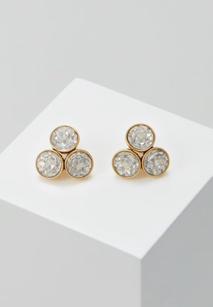 Paire de boucles d'oreilles en ton or avec trois pierres claires rondes facettées disposées en grappe triangulaire sur un socle blanc.