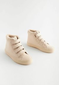 Beige high-top schoenen met een gestructureerde rubberen zool, nepveren voering en drie verstelbare klittenbandbanden aan de voorkant.