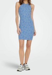 Femme portant une robe sans manches, bleu, arrivant au genou avec un imprimé floral blanc, associée à des baskets de sport blanches et grises.