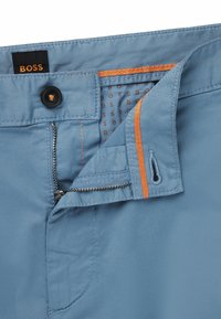 Blue trousers with a smooth texture, featuring an orange accent on the zipper area and a black label with the brand name "BOSS."