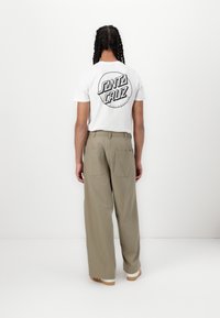 White short-sleeve t-shirt featuring black "Santa Cruz" logo on the back, paired with loose-fitting beige pants with two back pockets.