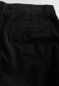 Black corduroy pants featuring vertical ribbed texture, a back pocket, and belt loops, with a clean finish along seams.