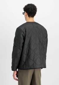 Veste noire matelassée avec un motif en vagues, dotée d'un col rond et d'une poche latérale. Le tissu semble lisse avec un léger éclat.