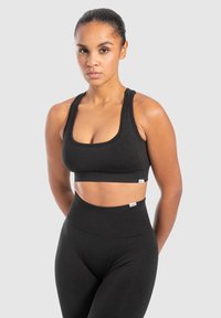 Schwarzer sportlicher Sport-BH mit breiten Schulterträgern und quadratischem Ausschnitt, kombiniert mit hochgeschnittenen schwarzen Leggings. Weicher, dehnbarem Stoff.