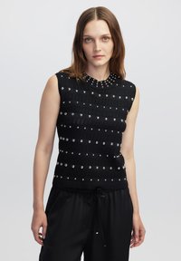 Top senza maniche in maglia nera con righe orizzontali, impreziosito con borchie argentate e scollatura rotonda, abbinato a pantaloni neri dalla vestibilità rilassata.