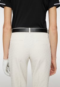 Black belt with a silver buckle worn with light-colored pants featuring a textured herringbone pattern and side pockets. White golf glove visible.