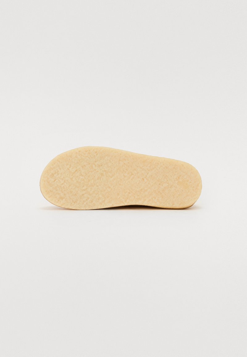 Zool van een schoen met een gestructureerd beige rubberen oppervlakte en een gladde, afgeronde rand. Geen zichtbare patronen of extra kenmerken.