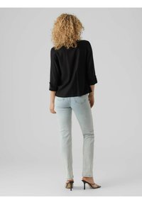 Svart topp med trekvartslånga ärmar och uppvikta ärmkanter, tillsammans med ljusblå skinny jeans och svarta klacksandaler, sedd bakifrån.