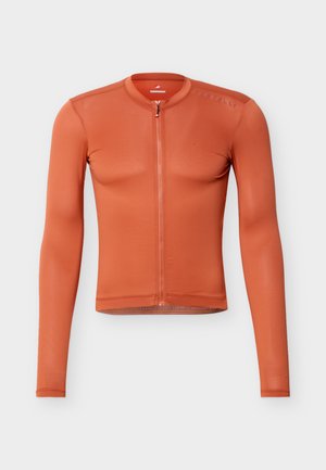 Langærmet, figursyet cykeltrøje i rustorange med fuld lynlås foran og subtilt tekstureret stof på en ensfarvet lys baggrund.
