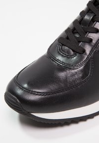 Černé kožené sneakersy s kulatou špičkou, texturovaným povrchem a černými tkaničkami. Disponují bílou mezipodešví a gumovou podrážkou s vzorkem.