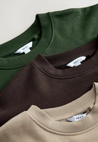 Tre crew-neck sweatshirts i mörkgrön, brun och beige. Tillverkade av mjukt material med ribbade kragar. Etiketter synliga.
