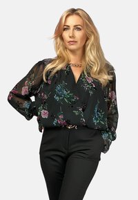 Czarna bluzka w kwiaty z przezroczystymi długimi rękawami, z wielokolorowymi wzorami kwiatowymi, luźny krój i głęboki dekolt w literę V, zestawiona z czarnymi spodniami.