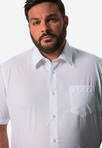 Camicia bianca a maniche corte con bottoni, realizzata in tessuto liscio, con colletto a punta e taschino sul lato sinistro del petto.