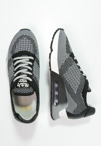 Černé a šedé pletené tenisky s tkaničkovým designem, mají texturovaný svršek, bílou mezipodešev a viditelné vzduchov é odpružení na patě.