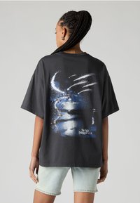 T-shirt de algodão preta com corte descontraído, apresentando uma impressão gráfica de uma cena ao luar com estrelas e o texto "A Noite Pertencia a Nós" em branco.