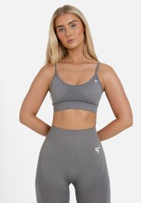 Top sportivo grigio con spalline sottili, design senza cuciture e texture leggera. Presenta un logo sul lato sinistro. Abbinato a leggings a vita alta coordinati.