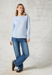 Ljusblå stickad tröja med rak skärning, som har en rund halsringning och knappar som accent på axeln; kombineras med ljusblå jeans och mörka skor.