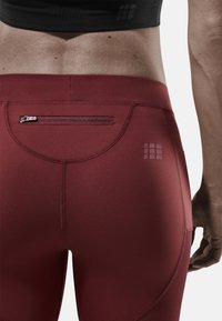 Rode hoge taille legging met een ritszak, gestructureerde naden en een subtiele merklogo aan de linkerkant. Glad, rekbaar materiaal.