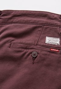 Pantalon Levi's marron avec poche arrière à fermeture par bouton, étiquette blanche Levi's et petite étiquette de marque rouge Levi's.