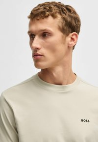 Lys beige crew-neck sweatshirt lavet af glat stof, med et lille sort "BOSS" logo på venstre bryst. Minimalistisk design, klassisk pasform.