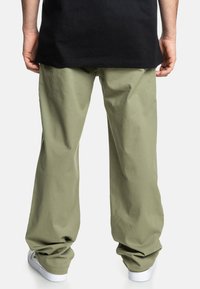 Lys grønne bomuldsbukser med en loose fit, der har et enkelt design og opsmøgte stile, parret med hvide sneakers.