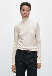 Beige coltrui gemaakt van zacht materiaal, met lange mouwen en een aansluitende pasvorm, gecombineerd met donkere denim jeans en een bruine riem.