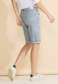 Raidallinen farkkushortsit käännetyllä helman, joissa on sivu- ja takataskut, yhdistetty valkoisiin lenkkareihin. Vaaleansininen ja valkoinen väriteema.