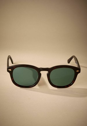 Tortoiseshell sunglasses with green lenses, square shape, and black arms. Notable detailing includes a small metallic accent on the frame.