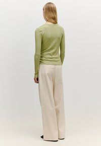 Langsleeve, geribbelde, olijfgroene top gecombineerd met brede, crème-kleurige broek. De outfit heeft een aansluitende silhouet met een zachte textuur.