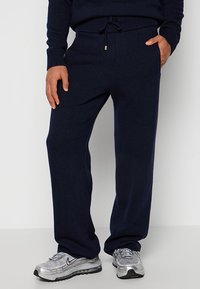 Marineblauwe gebreide joggers met een elastische tailleband en trekkoord, voorzien van zijzakken en een comfortabele pasvorm, gecombineerd met zilveren sportschoenen.