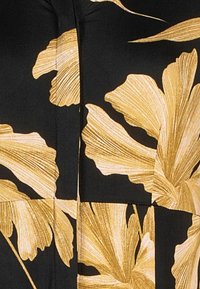 Czarny materiał z dużymi, szczegółowymi, złoto-żółtymi wzorami kwiatowymi, charakteryzującymi się zakrzywionymi płatkami i delikatnymi liniowymi fakturami.