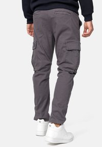 Pantalones cargo grises con bolsillos laterales, corte ajustado y material de mezcla de algodón resistente, combinados con zapatillas blancas.