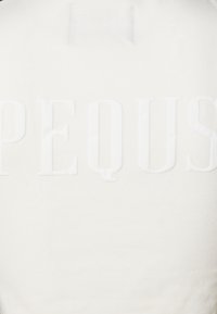 Vit sweatshirt med upphöjd blockbokstäver som stavar "PEQUUS." Tyget verkar mjukt med en slät textur, kompletterat av en enkel design.