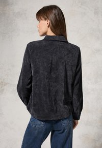 Black corduroy shirt with a collared neck, long sleeves, and a textured finish. The back features a relaxed fit and subtle stripe pattern.