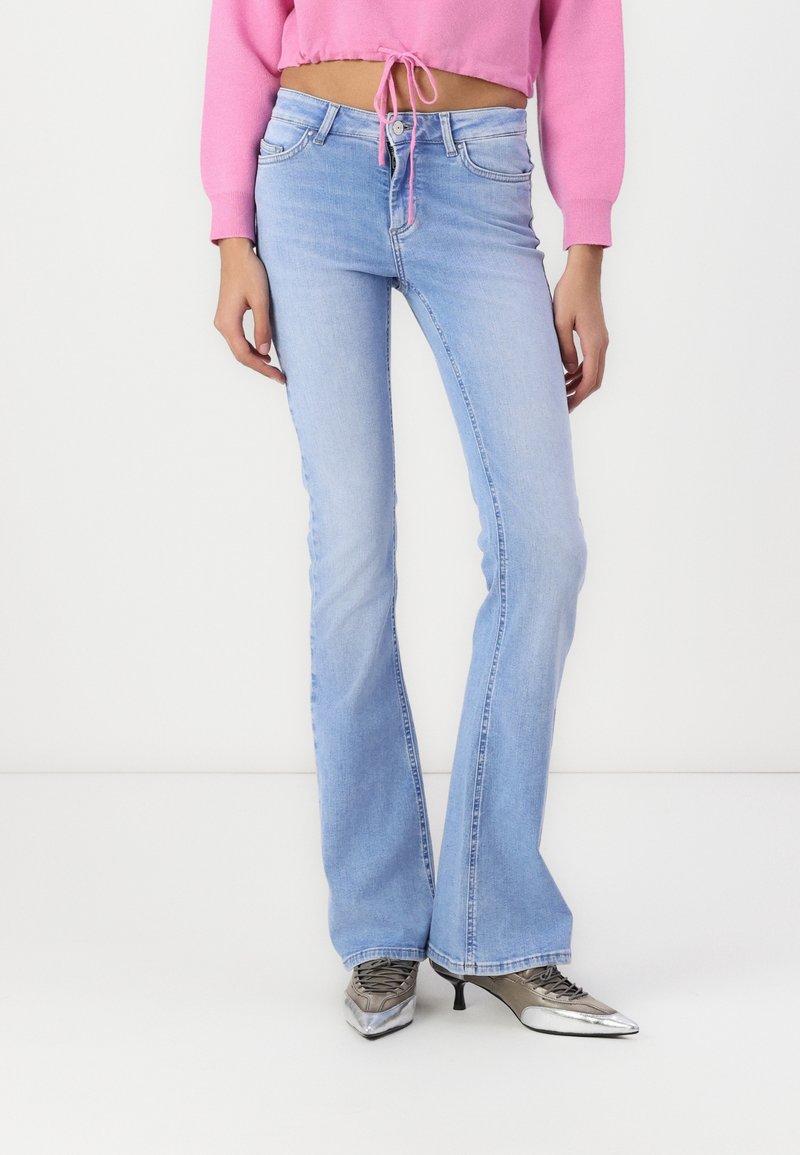 Ljusblå utsvängda jeans i denim, med subtil blekning, femfickorsdesign och medelhög midja, i kombination med silverfärgade skor.