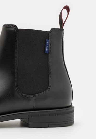 Black leather Chelsea boot with elastic panels, rounded toe, and a pull tab featuring a maroon accent. Subtle stitching detail.