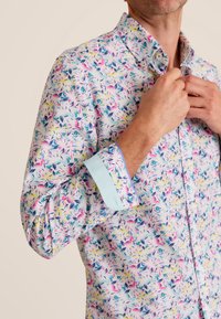 Overhemd met knoopsluiting met een bloemmotief in roze, geel en blauw op een lichte achtergrond. Inclusief een contrasterende lichtblauwe manchette.