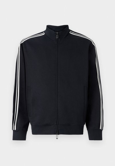 Schwarze Zip-Jacke aus strukturiertem Stoff mit weißen Seitenstreifen, hohem Kragen und gerippten Bündchen an den Ärmeln und am Saum.