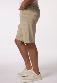Shorts beige realizzati in tessuto con una superficie liscia, dotati di tasche laterali e una vestibilità comoda, abbinati a sneakers grigio chiaro.