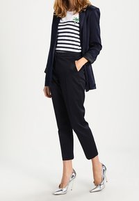 Blazer blu navy, top a righe bianche e blu navy, pantaloni neri a fantasia e tacchi alti argentati metallici. Presenta un dettaglio ricamato verde sul top.
