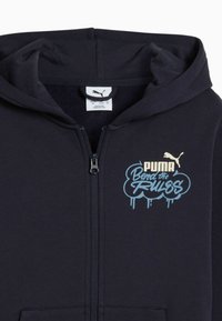 Felpa con zip di colore blu navy realizzata in tessuto morbido. Presenta un logo frontale in oro e blu chiaro con testo in stile graffiti. Include un cappuccio regolabile con cordino.
